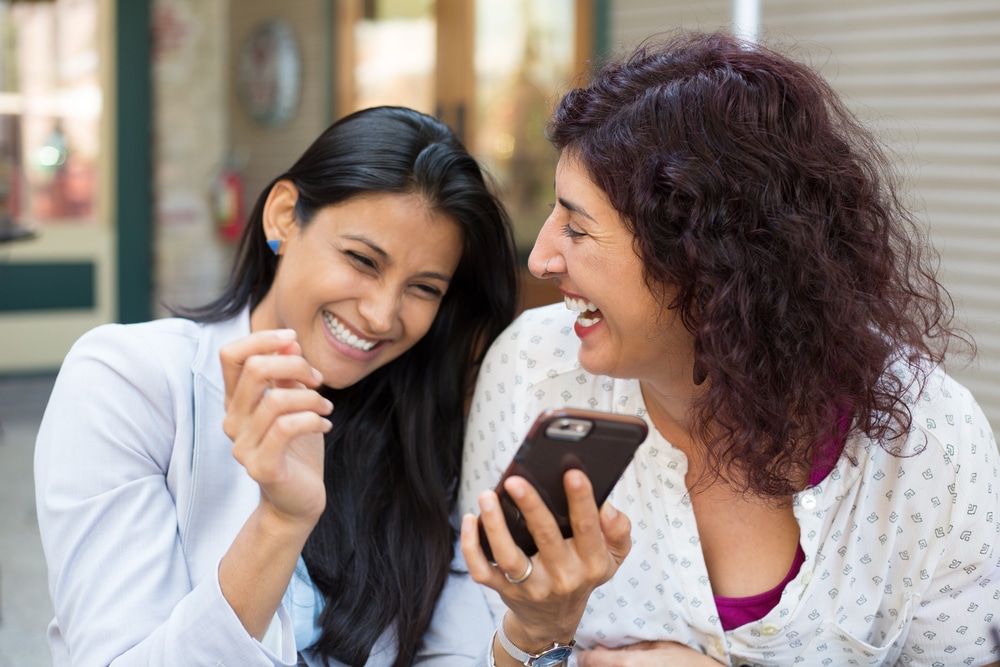 Zwei Frauen schauen auf ein Smartphone und lachen. Quelle: ashTproductions / Shuttersock