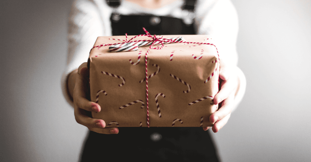 Abbildung: Eine Frau überreicht ein gepacktes Weihnachtsgeschenk – ein Symbolbild für die Geschenke, die wir euch für eure digitale Kommunikation machen
